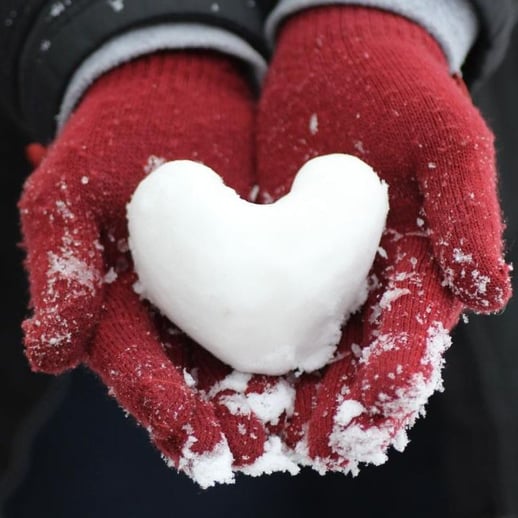 gloved hands holding a heart-shaped snowball
